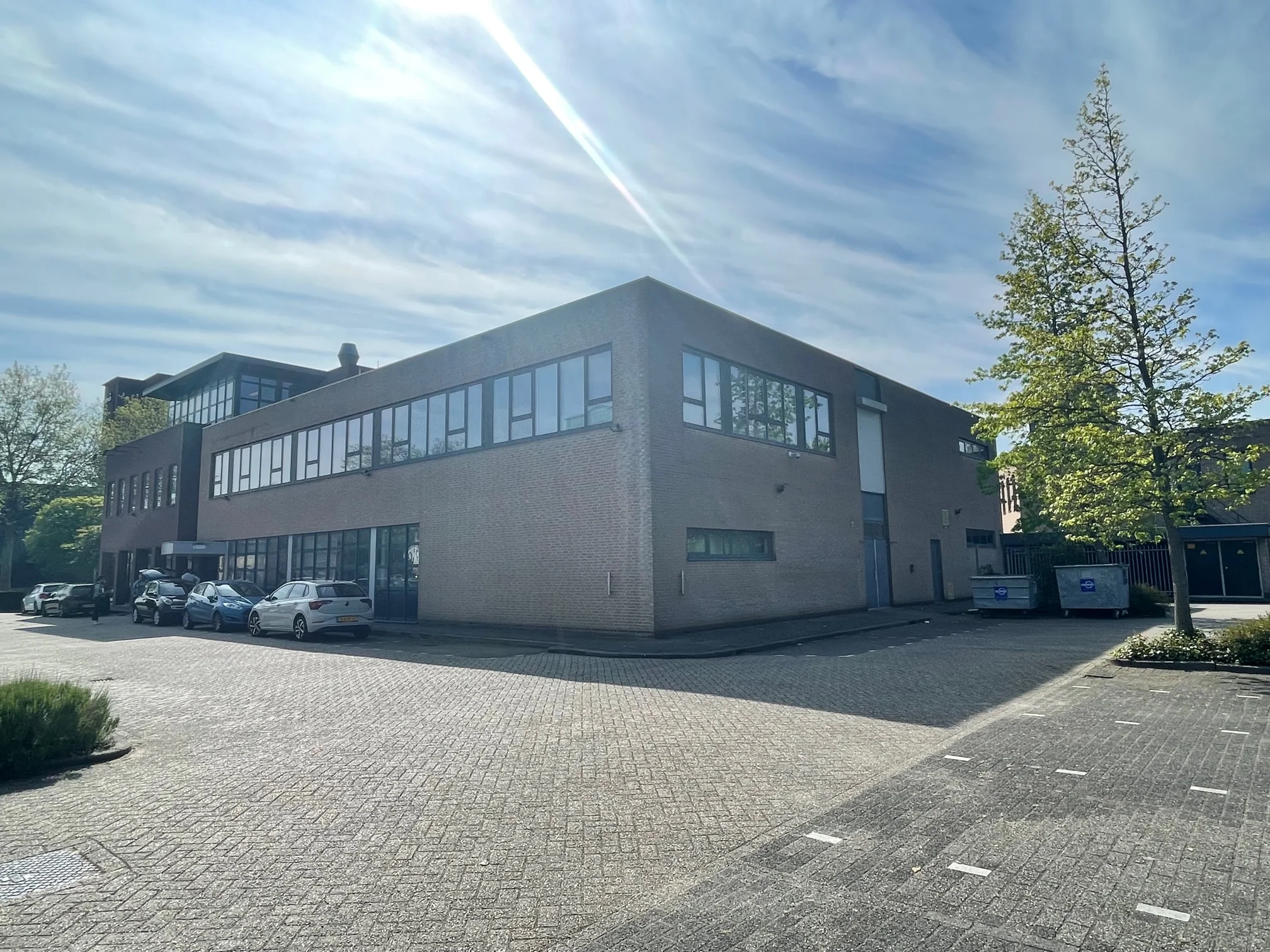 Bedrijfspand aan de Rivium 4e Straat met parkeerplaatsen en geparkeerde auto's op een zonnige dag.